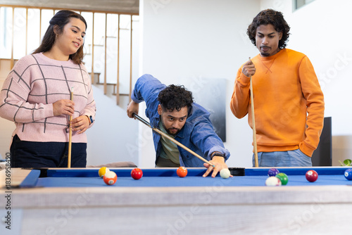Friends playing pool with cues and scattered balls around blue-felt billiard table in home rec room