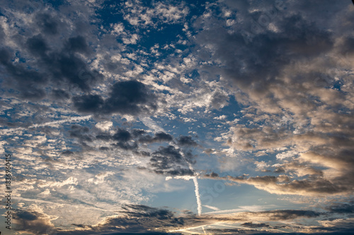 Vom Sonnenlicht angestrahlte Schicht-, Schleiher- und Schäfchenwolken mit sich kreuzenden Kondensstreifen am Abend- oder Morgenhimmel