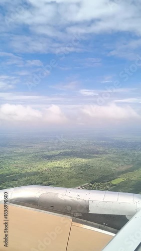 Vertical POV shot from airplane window flying above white clouds with blue sky and engine visible handheld