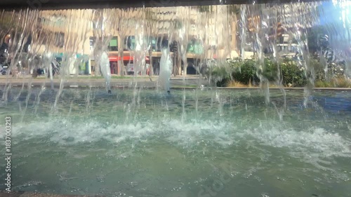 A view of traffic in a southern European city as seen through a wall of water falling from a city fountain.