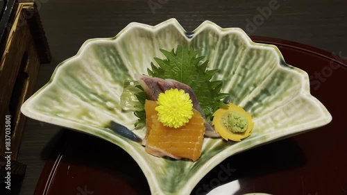 Exquisitely plated sashimi on a leaf-shaped dish, garnished with flowers.