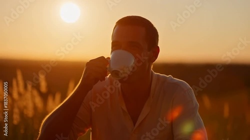 Man smiling while drinking coffee outdoors at sunset in field