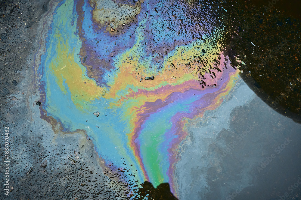 Naklejka premium Oil Spill Creates Colorful Reflection on Pavement During Daylight at Urban Location