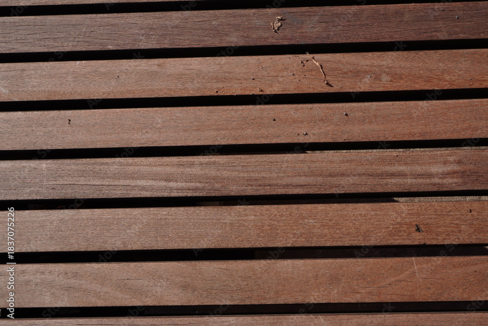 Fototapeta premium An architectural close-up of horizontal reddish-brown wooden slats, featuring a fine natural grain, uniform spacing, and rhythmic linear shadows between the planks.