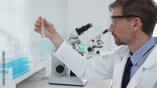 Male scientist in a white lab coat and protective glasses is analyzing a liquid in a test tube within a laboratory setting. Medicine, healthcare and science concept