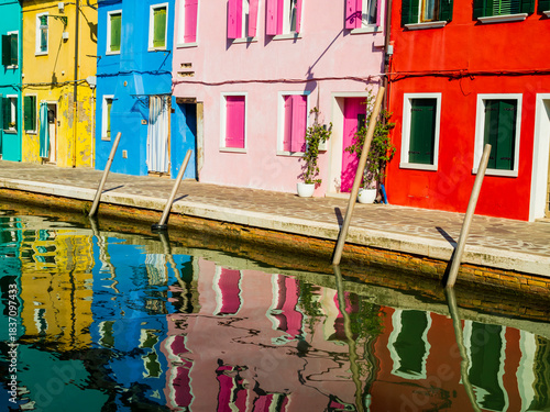 Row of brightly colored houses reflected in the calm canals of Burano, Venice, Italy