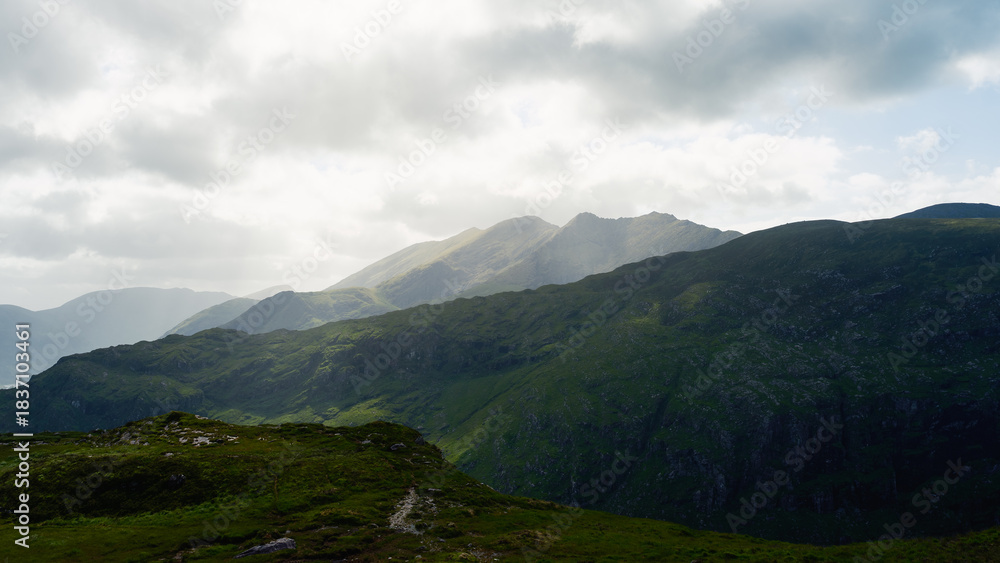 Fototapeta premium Picturesque mountain vista. Green hills and valleys under a soft light. The view invites exploration and relaxation. Ideal for travel websites or promotional materials.