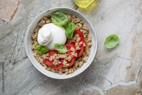 Quinoa bowl with tomatoes and burrata cheese on a grey granite background, horizontal shot, flat lay