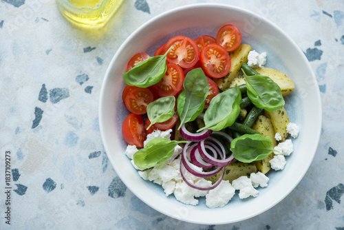 Plate of potato salad with cherry tomatoes, ricotta and fresh basil, horizontal shot on a white and blue granite background, high angle view