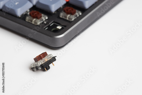 Mechanical keyboard with a removed brown switch placed on white surface, showing socket and switch details

