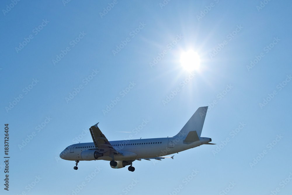 Obraz premium White Passenger Airplane Flying in Clear Blue Sky with Bright Sun Flare
