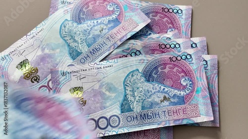 A close-up of ten thousand Kazakhstani tenge banknotes with an image of a snow leopard falling one by one onto the table