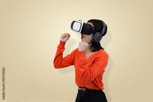 young Asian woman in an orange sweater wearing a virtual reality headset and headphones, symbolizing amazement or surprised within an immersive virtual environment in studio background
