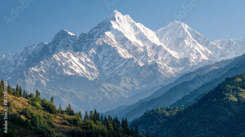 Wallpaper Mural Stunning snow-capped mountain peaks towering above lush green forested hills under a clear blue sky in a breathtaking natural landscape scene Torontodigital.ca