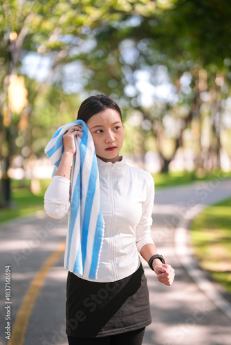 Photos Asian woman wipes sweat from face with towel after outdoor fitness exercise in p