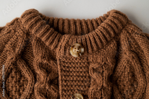 Close-up of brown knitted wool cotton sweater. Details of cozy winter or fall children's sweater, buttoned cardigan, pullover. Neckline detail, sleeves, large knit pattern. Trendy Color 2025