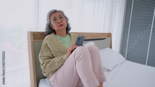 Serene Contemplation: An elderly woman is deeply immersed in her thoughts, cradling a cell phone in her hands while seated on the bed. Reflecting the calm nature of inner self