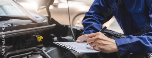 Auto check up and car service shop concept. Mechanic writing job checklist to clipboard to estimate repair quotation to client at workshop garage.