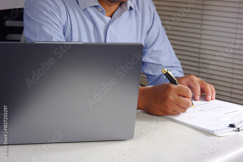 A person looks at a chart report on a laptop and then checks off the task list and budget list. Checks all the status checklist boxes and then signs it. The concept of checking and approving
