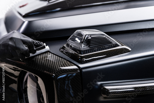 Close-up of ceramic coating being applied to a carbon fiber exterior element on a luxury car, highlighting precision work, surface protection, deep gloss and premium car detailing service.