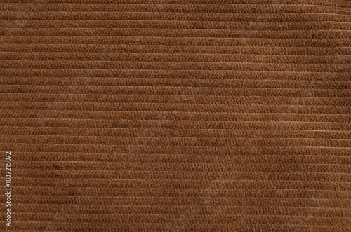 Close-up of texture of brown ribbed cotton corduroy fabric. Abstract textile background, warm and cozy material for fall clothing, shirts, pants, skirts, and jackets. Soft velvety fabric