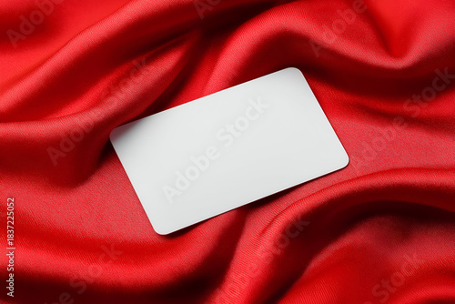 A blank card resting elegantly on smooth red silk fabric, perfect for customized designs or marketing materials.