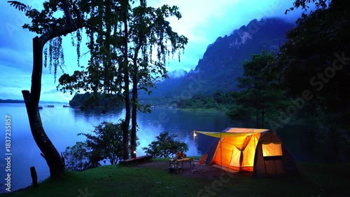 Night camping in a forest with a tent under the sky surrounded by trees and mountains