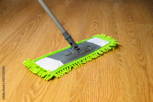 A green microfiber flat mop glides across a wooden floor, capturing dust and maintaining cleanliness.