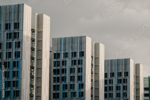 A row of modern apartment buildings with blue accents under a cloudy sky. The buildings are tall and feature a grid-like facade.