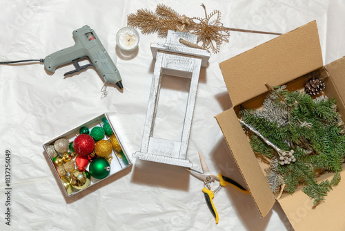 Top view of a table with materials for making a handmade decorative candle holder, scissors, glue gun, branches, Christmas balls, cones. The concept of decorating a house for a holiday.