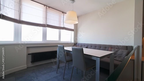 Modern dining area with large windows, gray chairs, table, and radiator, creating a bright and minimalist interior design.