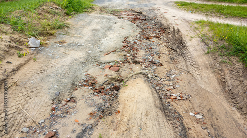 Washed-out dirt road after heavy rains with traces of water, old bricks, stones, gravel and sand.