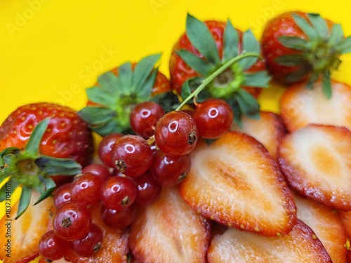 Portion of red currant and strawberries against a yellow background