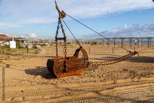 Fototapeta Naklejka Na Ścianę i Meble -  A large dragline bucket on a beach at sunset, used for dredging sand and gravel in coastal reinforcement work before the tourist season. Evrenseki, Antalya, Turkey, Mediterranean.