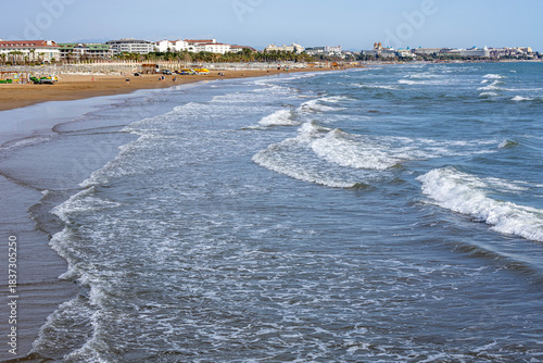 Fototapeta Naklejka Na Ścianę i Meble -  A serene, empty beach with rolling white-capped waves under a spring sun, its infrastructure not yet ready for the high season. A peaceful interlude on the Mediterranean coast. Evrenseki, Antalya, Tur