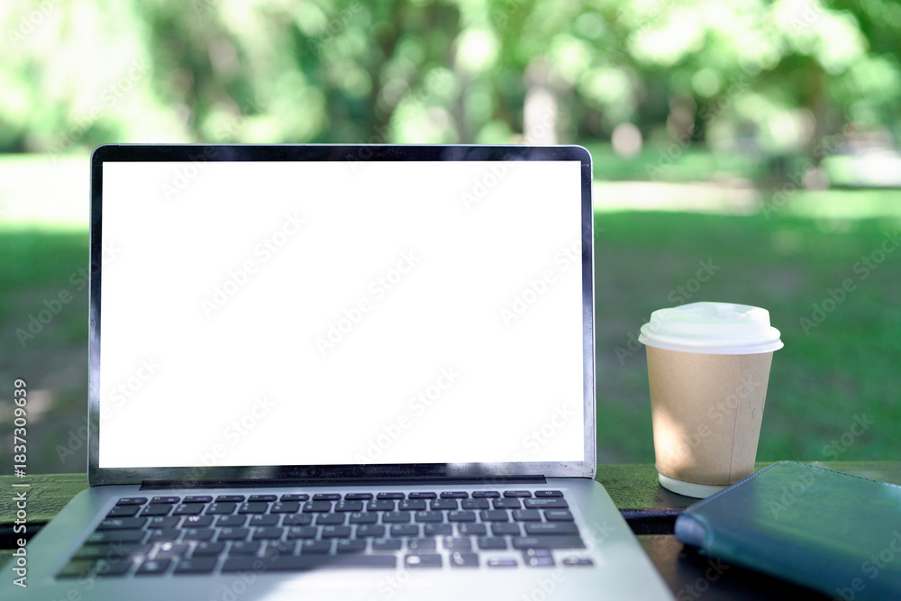 Fototapeta premium Mock up laptop computer, coffee cup on wooden table in the green garden.