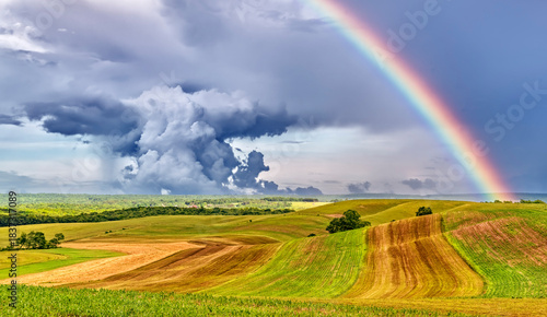 фотографія rainbow over hilly fields and farmlands with thunderhead cloud and rains at the