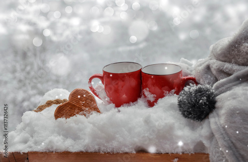 two red mugs with wooden  heart shaped in the snow with blanket on bright  lights bokeh background
