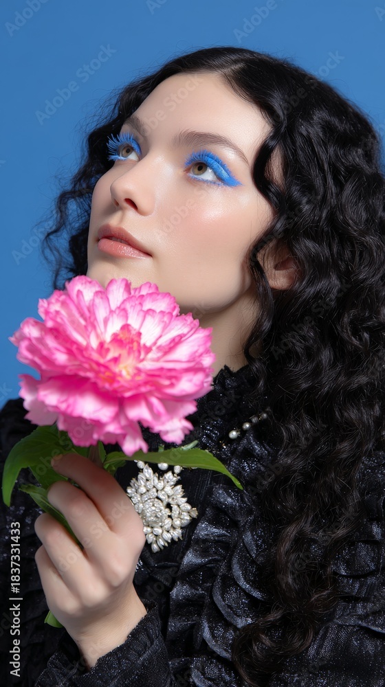 Naklejka premium Young caucasian female with curly hair holding pink flower on blue background