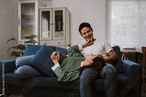 Asian couple resting and smiling on a sofa, enjoying each other's company in a comfortable home interior