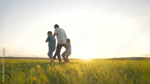 Happy team play.Group of children on grass in park. Boys and girls play with ball at sunset in park.Active team plays with ball in summer.Schoolchildren rest in nature.Children play football with ball