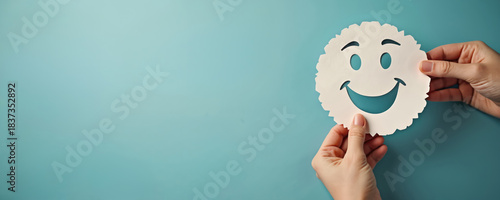 Hands hold paper smile face on blue. Positive thinking, world mental health day concept. Paper cut out face shows good mood and happiness. Happy client feedback review symbol.