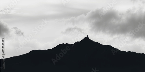 A breathtaking view of the snow-covered peak of an Alp mountain as the sun sets, casting a silhouette against a cloudy sky over the landscape