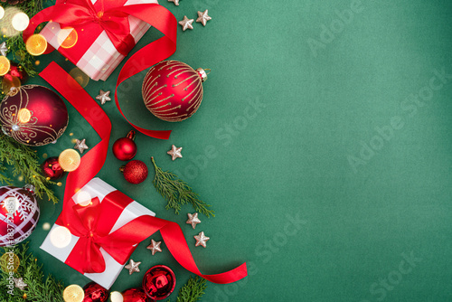 Holiday flat lay with red and white wrapped gifts, baubles, ribbon, stars, and greenery on a green background.