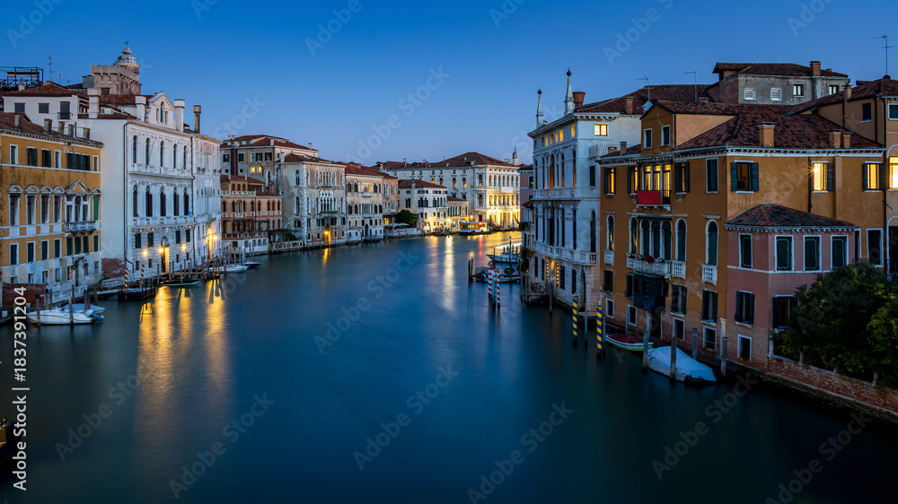 Fototapeta premium Morning in Venice - view from the Accademia Bridge on the Grand Canal, reflecting the lights from the surrounding houses and the blue sky - long exposure
