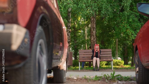 low road view car wheel passing caucasian skater on bench, spinning tire close to frame, motion blur and sudden tension, bench and birch trees in background, startled reaction and urban hazard