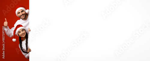 Two friends show excitement during the holiday season, wearing festive Santa hats. They stand against a bright red background and express joy with playful gestures.