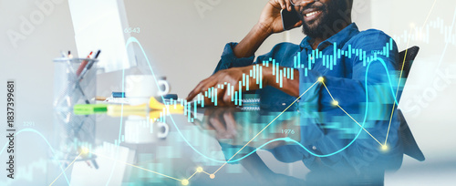 A business professional sits at a desk while holding a phone to his ear, reviewing market data displayed on a screen. Various charts and graphs surrounding him suggest active analysis.