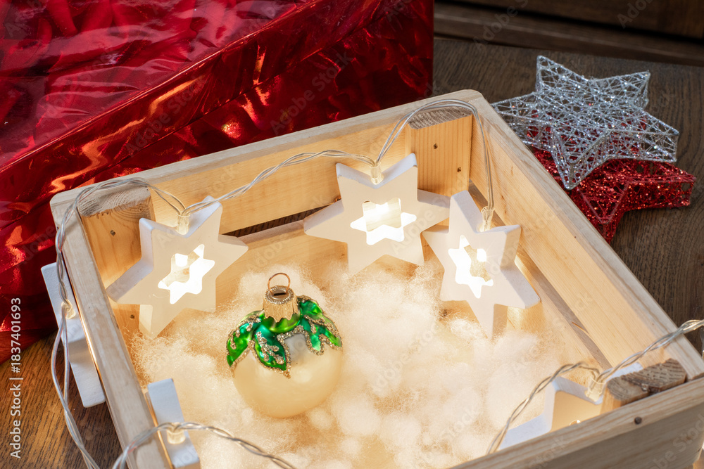 Fototapeta premium Wooden crate with glowing star lights and Christmas ornament on fluffy white artificial snow. Holiday decor, festive display, seasonal lighting. Real photo