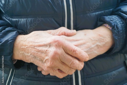 Übereinander geschlagene Hände von alter stehender Frau mit blauer Winterjacke 